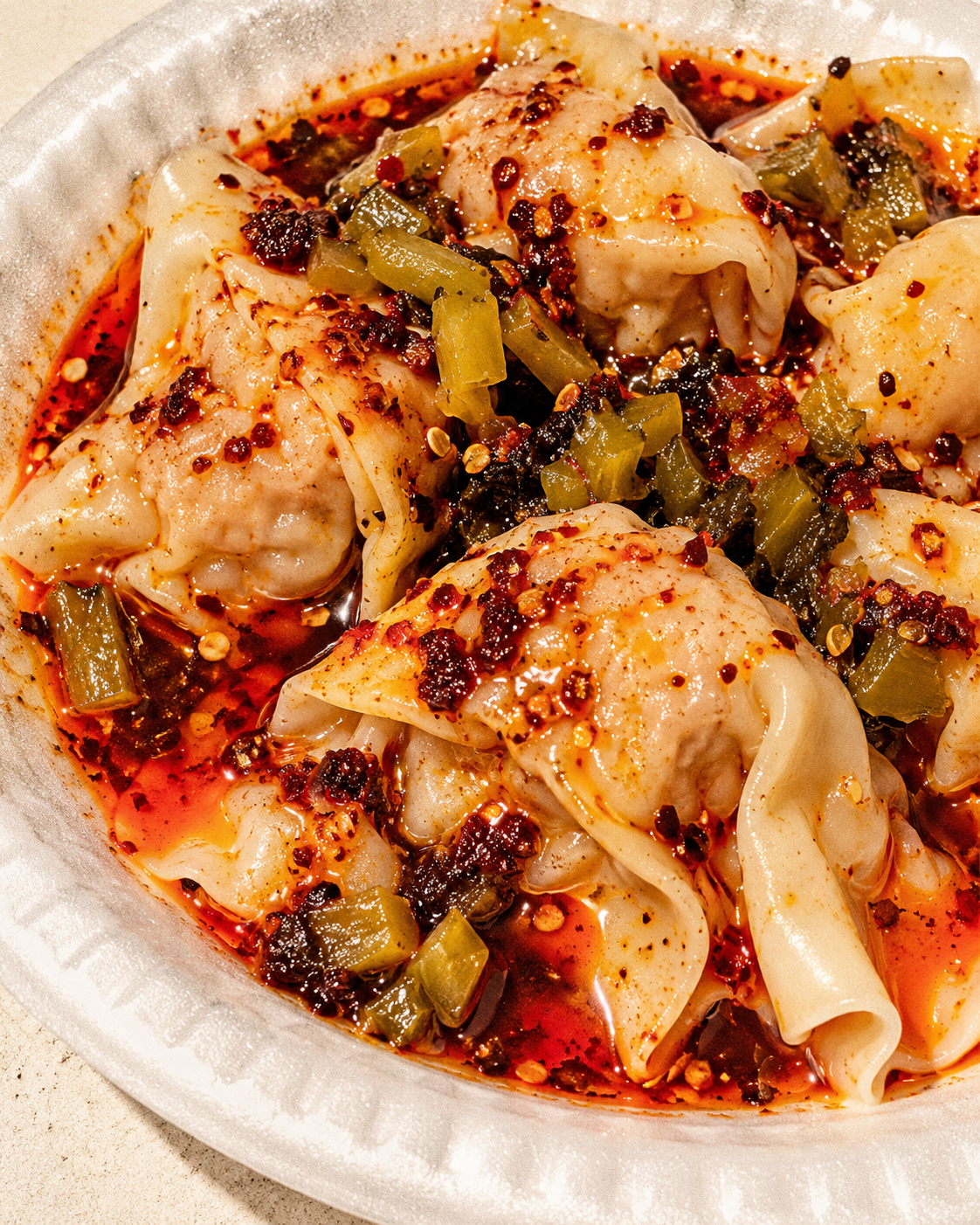 Pork wontons with chili oil and diced pickled greens, illustrative image